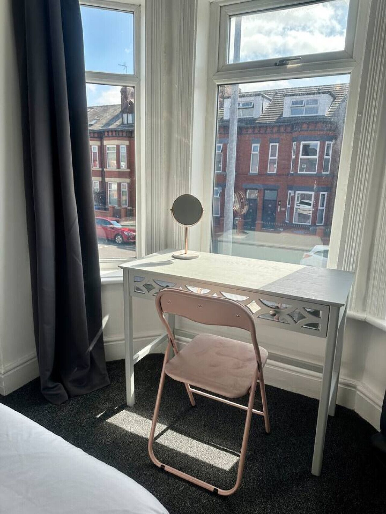 Ein kleines Hotelzimmer mit Schreibtisch, Stuhl und Fenster mit Blick auf die Straße.