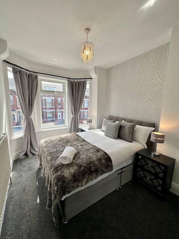 Ein modernes Schlafzimmer mit einem großen Bett, einer Kristallleuchter und Blick auf die Stadt durch das Fenster.
