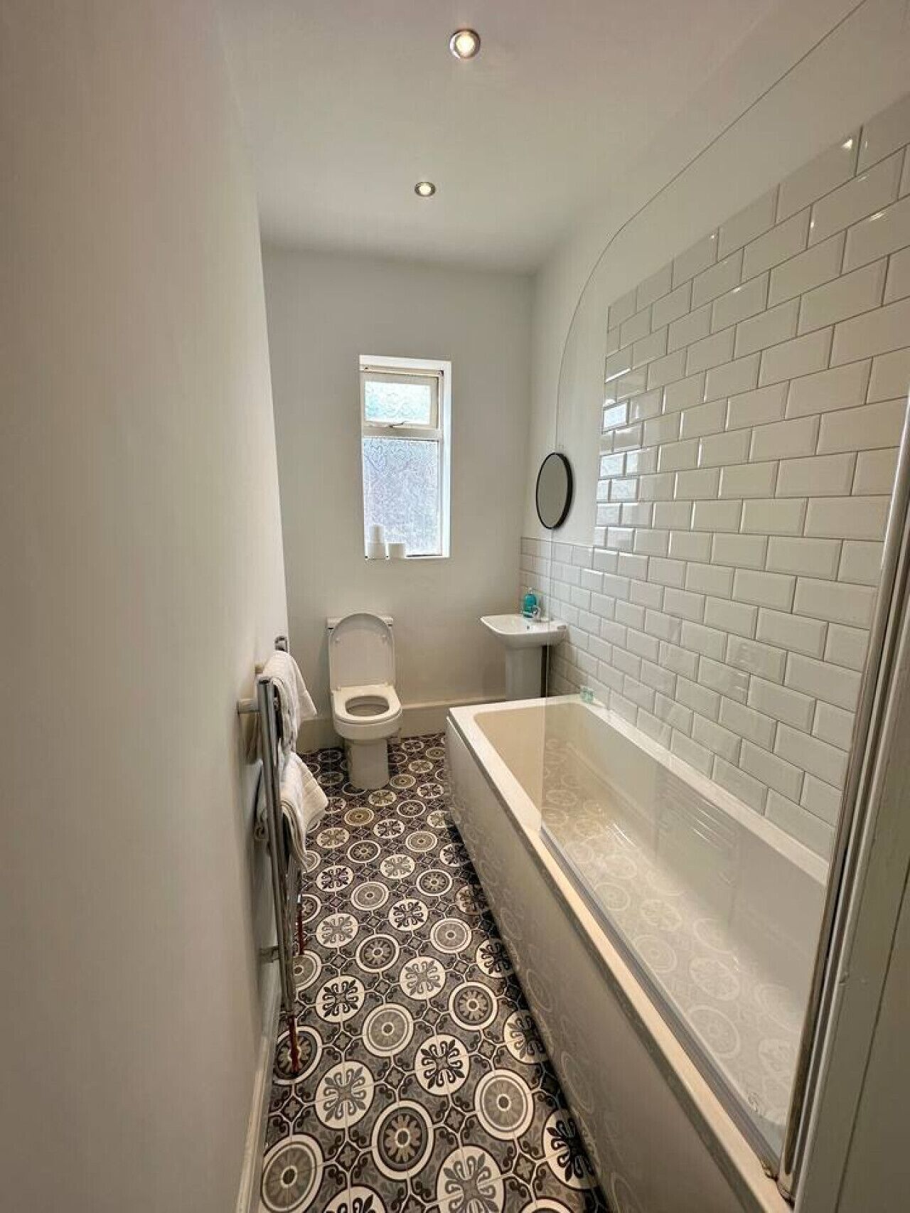 A bathroom with a patterned floor, a bathtub, a toilet, and a window.