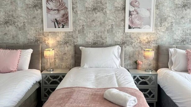 Ein Schlafzimmer mit zwei Betten, einer grauen Wand mit Struktur und gerahmten Bildern über jedem Bett.
