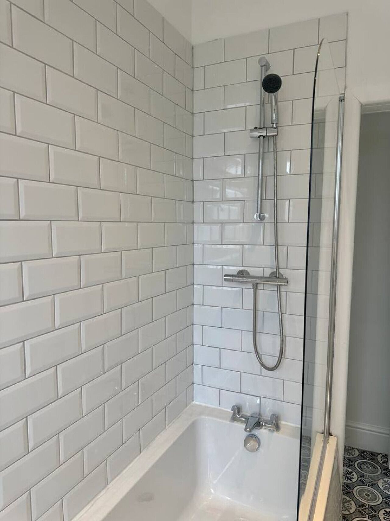Ein Badezimmer mit weißen Fliesen im U-Bahn-Stil, einer Glaskabine für die Dusche und einer weißen Badewanne.