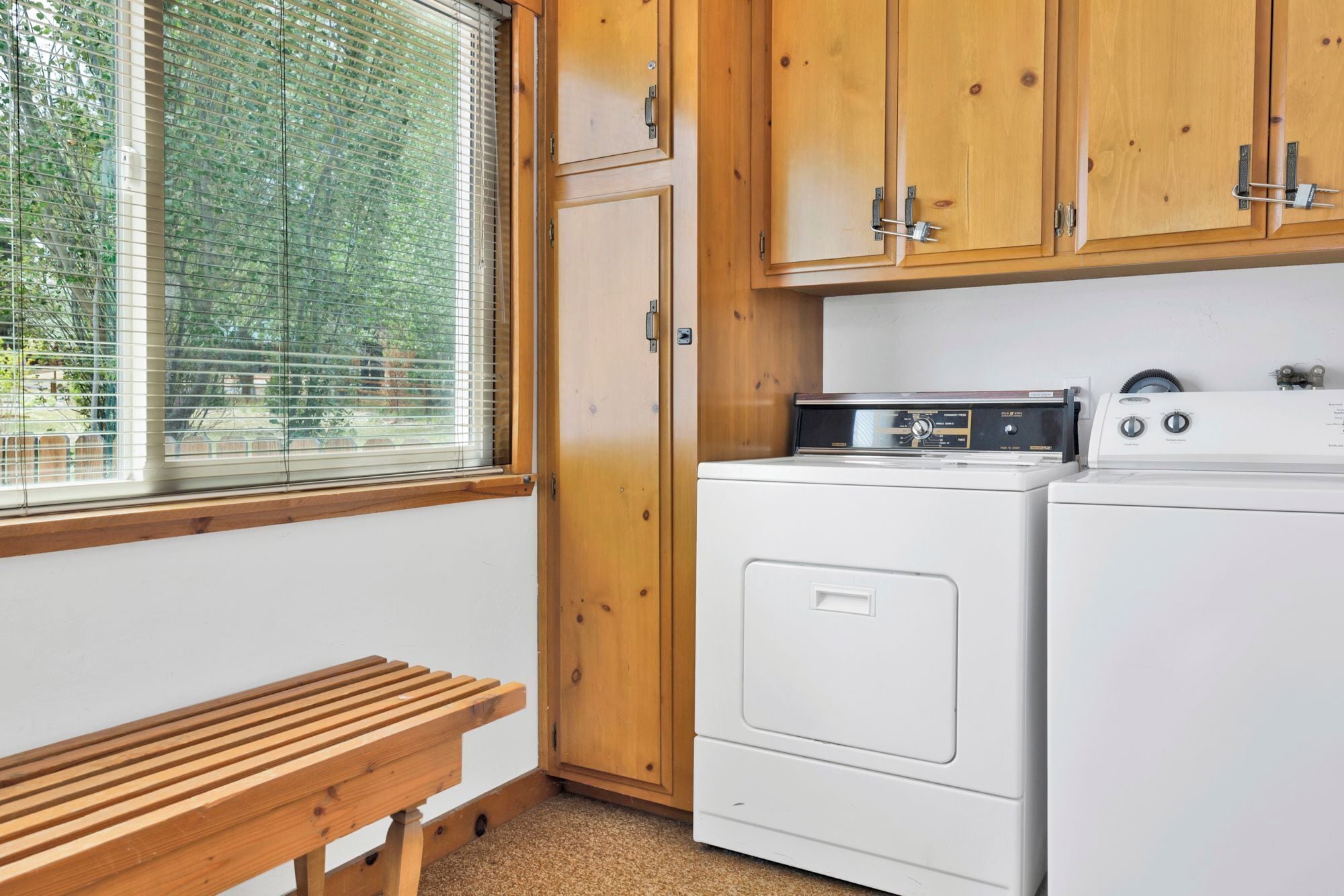 A laundry room with wooden cabinets, a washing machine, a dryer, and a bench.