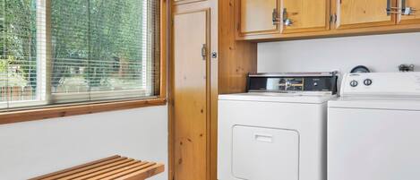 A laundry room with wooden cabinets, a washing machine, a dryer, and a bench.