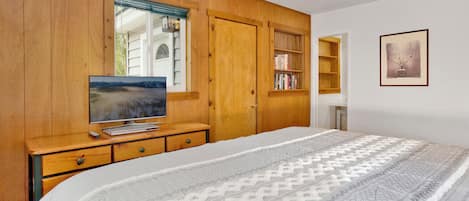 Un dormitorio con una cama grande, un armario de madera, un televisor sobre un aparador de madera, una estantería y un cuadro en la pared.