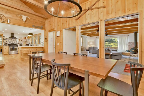 A spacious wooden interior with a large dining table, modern kitchen, and a cozy living area with a fireplace. - BOW Canyon Cabin #2172 (Big Bear Lake)
