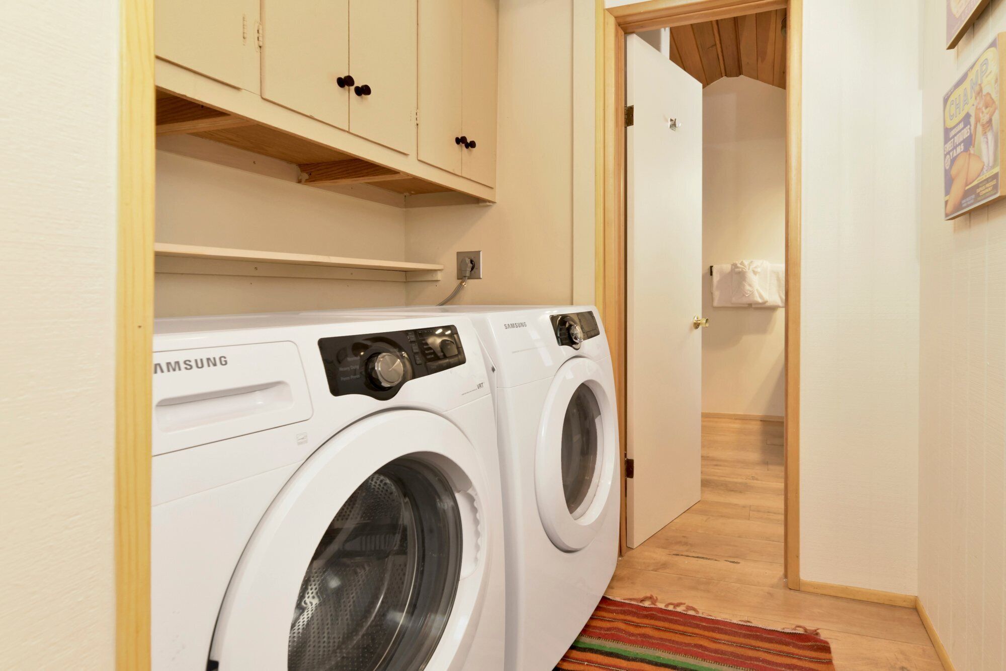 A laundry area with a Samsung front-loading washer and dryer, wooden cabinets, and a door leading to another room.