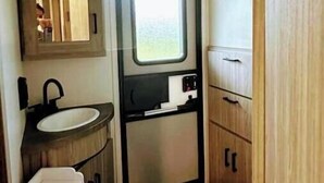 A compact RV bathroom with a sink, mirror, toilet, and storage cabinets. - City-Accessible Camper (Goldston)