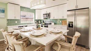 Una cocina moderna con armarios blancos, un refrigerador de acero inoxidable y un comedor con sillas de madera y una isla blanca.