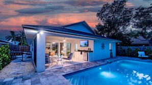 Una casa con piscina, un patio cubierto y vista al océano al atardecer.
