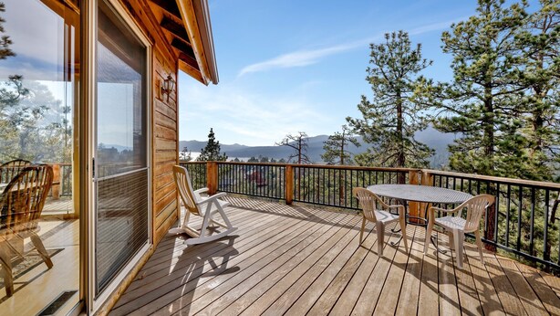 Une terrasse en bois avec une table et des chaises, offrant une vue sur un paysage montagneux.