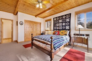 Ein Schlafzimmer mit Holzbalkendecke, einem großen Bett mit einem blumengemusterten Kopfteil, einer Steppdecke und einer Wandtasche mit Quilted-Optik.