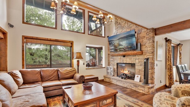 A cozy living room with a stone fireplace, leather sofa, and a large window overlooking greenery. - Luxury Lodge #1888 (Big Bear Lake)