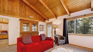 A cozy living room with a red sofa, a wooden cabinet, a grey armchair, and a large window with a view of trees. - Moulin Rouge #2055 (Big Bear Lake)