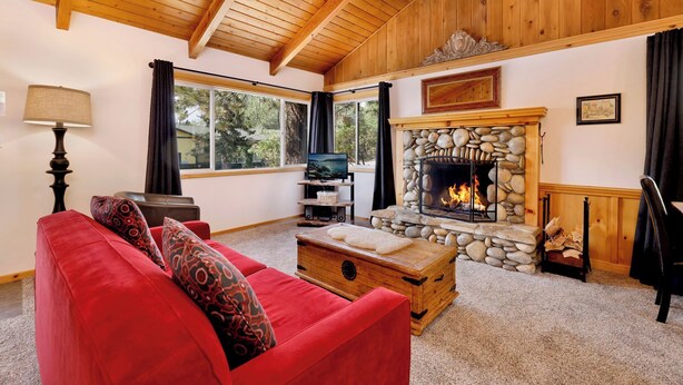 A cozy living room with a stone fireplace, a red sofa, and a television on a wooden stand. - Moulin Rouge #2055 (Big Bear Lake)