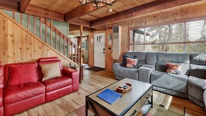 A wooden interior with a red leather sofa, a grey sectional sofa, and a glass coffee table. - Alpine Adventure #2166 (Big Bear City)