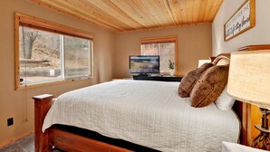 A bedroom with a large bed, wooden ceiling, two windows, a TV, and a bedside lamp. - Alpine Adventure #2166 (Big Bear City)