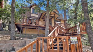 A cabin with a wooden staircase leading to a deck, surrounded by trees. - Alpine Adventure #2166 (Big Bear City)