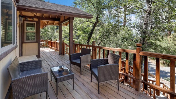 A wooden deck with wicker furniture and a covered area, surrounded by trees. - Alpine Adventure #2166 (Big Bear City)