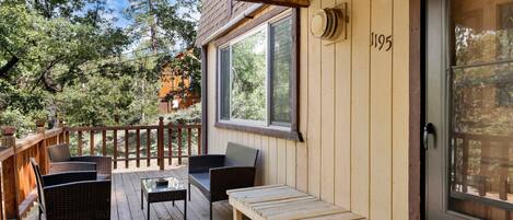 Una terraza de madera con mobiliario de mimbre, un banco y una puerta con el número 1195.