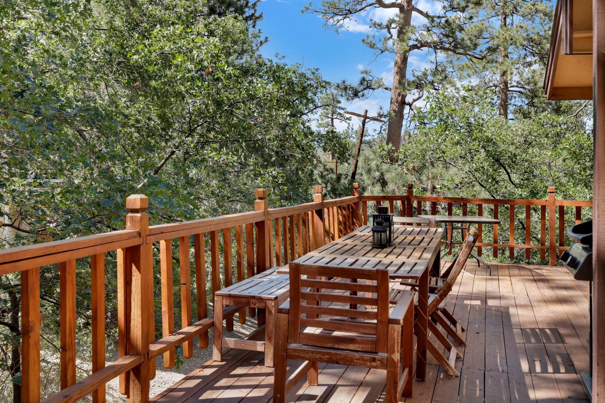 Um deck de madeira com mesa e cadeiras, cercado por um corrimão de madeira, com vista para uma área arborizada.