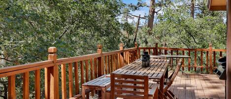 A wooden deck with a table and chairs, surrounded by a wooden railing, overlooking a forested area.