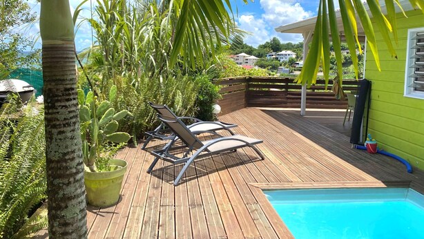 A wooden deck with a pool, surrounded by lush greenery and a clear blue sky. - VILLA ANAIS sea view, Trois Ilets, quiet, swimming pool, close to shops  (LES TROIS ILETS)