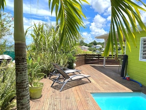 A wooden deck with a pool, surrounded by lush greenery and a clear blue sky.