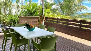 An outdoor seating area with a table and chairs, a bowl of fruit, and a view of tropical plants and a wooden fence. - VILLA ANAIS sea view, Trois Ilets, quiet, swimming pool, close to shops  (LES TROIS ILETS)