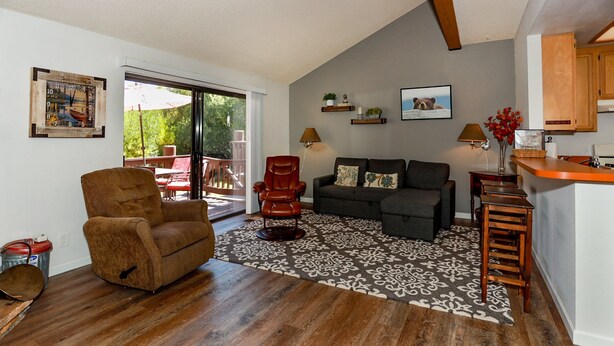 A living room with a brown leather chair, a dark grey sofa, and a patterned rug. There are wooden shelves with decorative items and a wooden cabinet. - Cienega Getaway #1952 (Big Bear Lake)