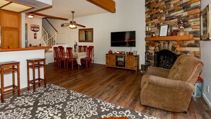 A living room with a fireplace, a TV, wooden furniture, and a staircase leading to another room. - Cienega Getaway #1952 (Big Bear Lake)