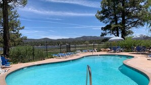 A swimming pool with a curved edge, surrounded by lounge chairs and umbrellas, with a mountainous backdrop. - Cienega Getaway #1952 (Big Bear Lake)