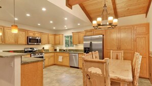 A spacious kitchen with wooden cabinets, a central island, stainless steel appliances, and a chandelier. - LA Cerena Getaway #1960 (Big Bear Lake)