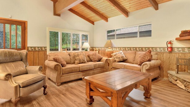 A spacious living room with a high wooden ceiling, a leather armchair, a beige sofa set, and a wooden coffee table. - LA Cerena Getaway #1960 (Big Bear Lake)