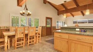 A spacious kitchen with wooden cabinets, a granite countertop, and a dining area with wooden chairs. - LA Cerena Getaway #1960 (Big Bear Lake)