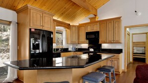 A kitchen with wooden cabinets, a black refrigerator, a microwave, and a large island with stools. - Shasta Mountain Cabin#1916 (Big Bear City)