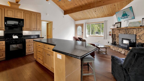 A spacious kitchen with wooden cabinets, a large island, and a stone fireplace. - Shasta Mountain Cabin#1916 (Big Bear City)