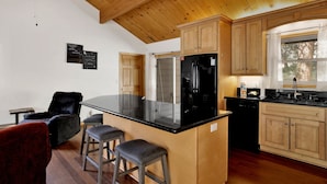 A kitchen with wooden cabinets, a black refrigerator, and a bar area with stools. - Shasta Mountain Cabin#1916 (Big Bear City)