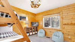 A cozy cabin room with a bunk bed, a television, a lamp, and a window with a view of trees. - Crescenta Pines LOG Cabin #2346 (Big Bear City)