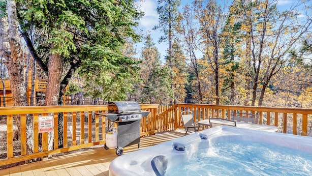 A wooden deck with a hot tub, a grill, and a table with chairs. - Crescenta Pines LOG Cabin #2346 (Big Bear City)