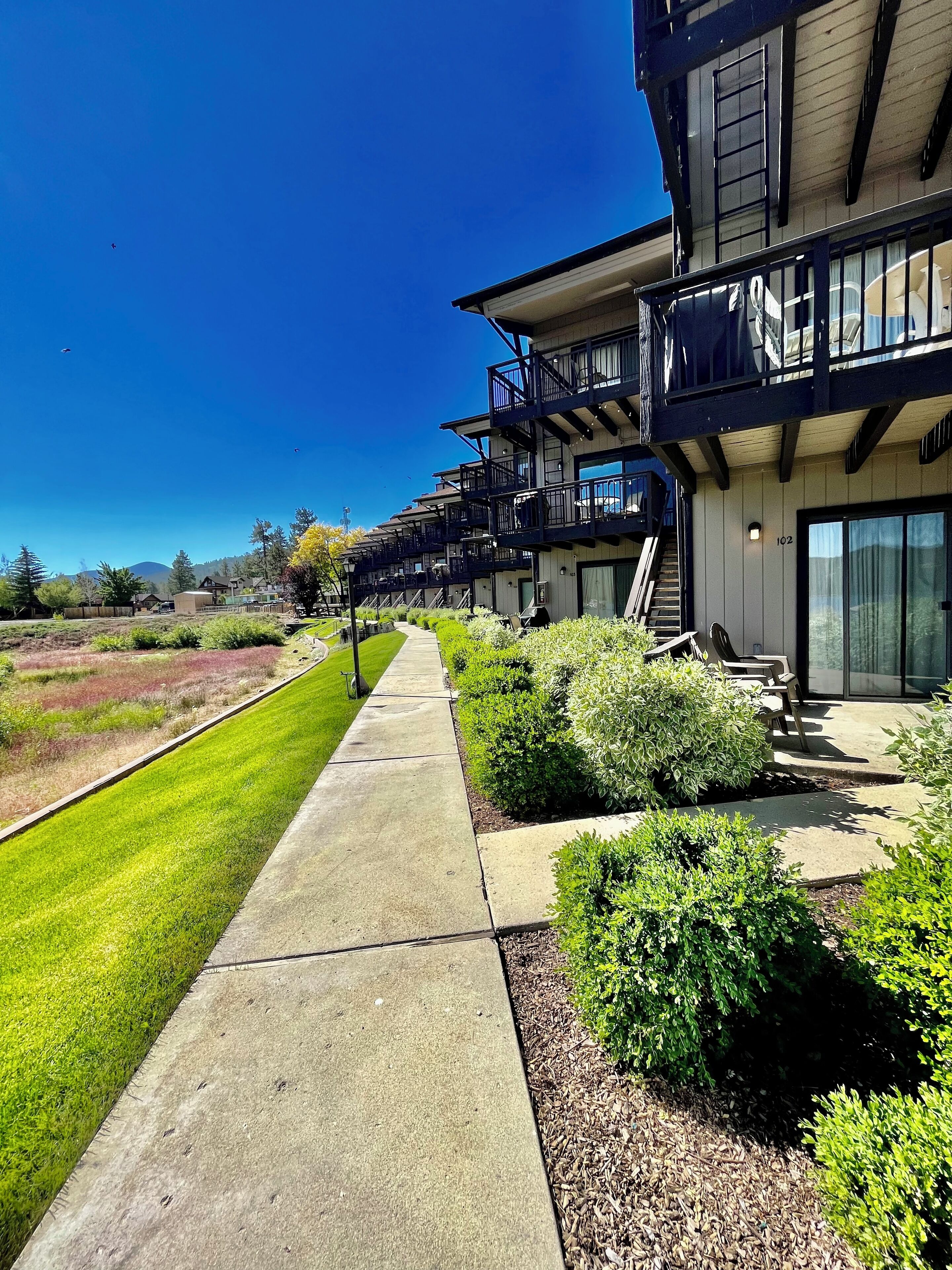 A modern building with multiple balconies, a well-maintained lawn, and a clear sky.