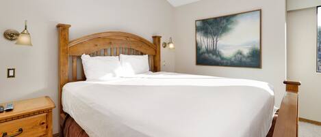 Una cama bien hecha en una habitación con cabecera de madera, una mesita de noche con control remoto y un cuadro en la pared.