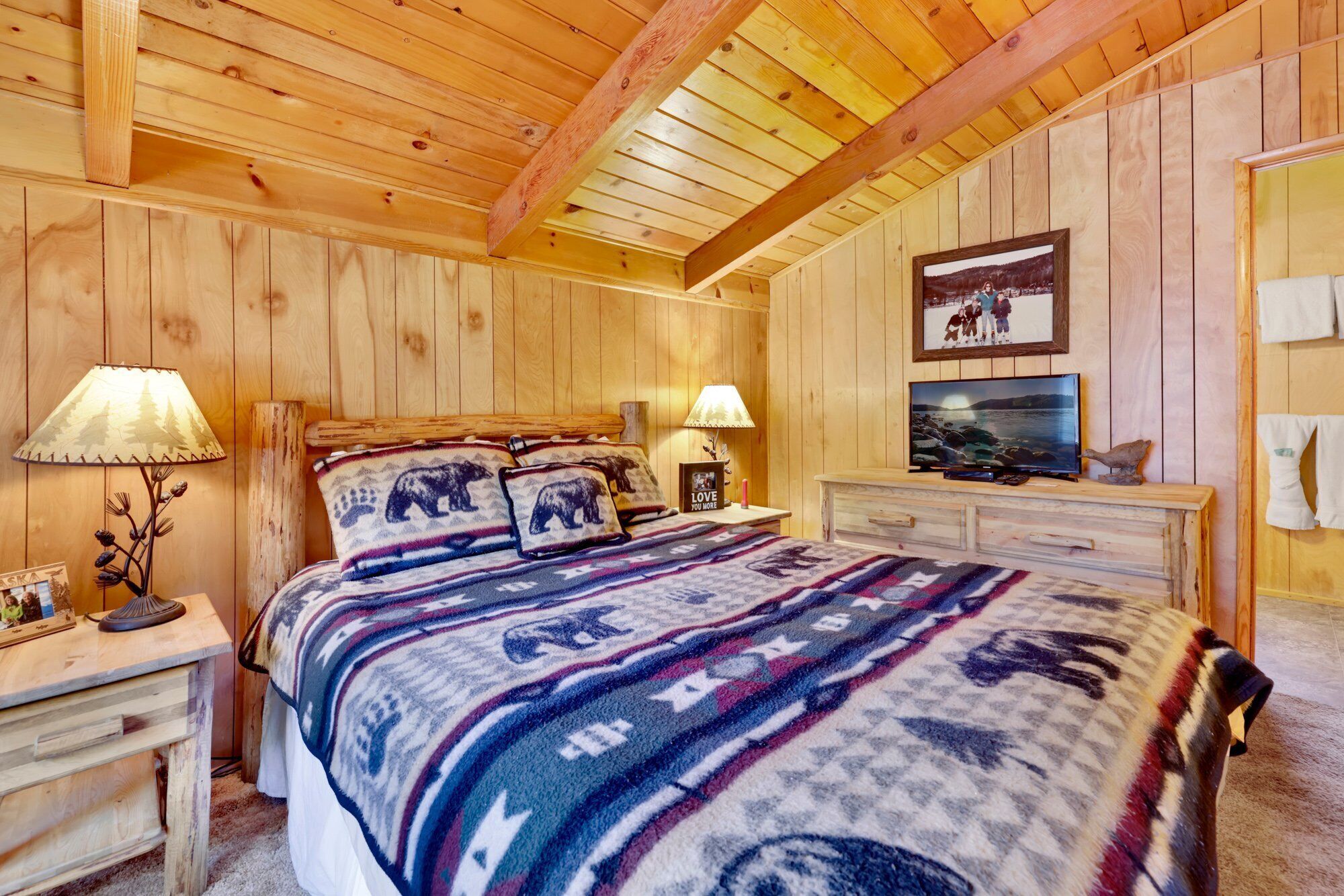Une pièce chaleureuse aux murs en bois, avec un lit, deux lampes de chevet, une télévision et une photo encadrée accrochée au mur.