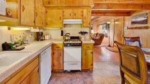 A cabin kitchen with wooden cabinets, a stove, and a dining area with a chair and table. - Paradise IN Cedar #2095 (Big Bear Lake)