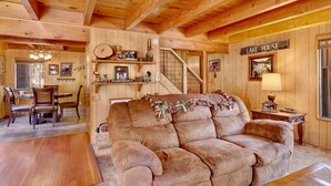 A cozy cabin interior with a wooden ceiling, a couch, a dining area, and a staircase. - Paradise IN Cedar #2095 (Big Bear Lake)