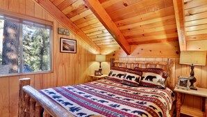 A cozy cabin bedroom with a wooden ceiling, a large window, a bed with a patterned blanket, and two bedside lamps. - Paradise IN Cedar #2095 (Big Bear Lake)