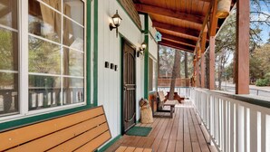 A wooden deck with benches and a covered area, a dog sitting by the door, and a view of trees and a street. - Whiskey Mountain Lodge - 2028 (Sugarloaf)