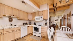 A kitchen with wooden cabinets, a microwave, a stove, and a dining area with a table and chairs. - Whiskey Mountain Lodge - 2028 (Sugarloaf)
