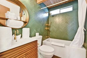 A bathroom with a herringbone-patterned green wall, a wooden vanity, a white sink, a toilet, and a bathtub with a showerhead. - Quail's Call #2415 (Big Bear Lake)