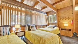 A wooden cabin room with two beds, a nightstand with a lamp, a small wooden cabinet, and a fire extinguisher on the wall. - Quail's Call #2415 (Big Bear Lake)