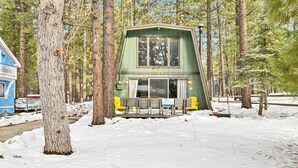 A cabin with a large window and a door, surrounded by trees and snow. - Quail's Call #2415 (Big Bear Lake)